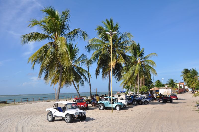 Praia com areia, mangue do lado e o mar ao fundo.